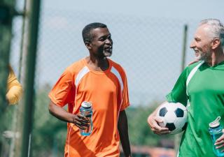 group of interracial elderly sportsmen with sportive water bottles walking on football field
